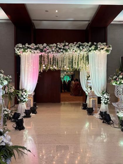 A classic entrance with a canopy of hanging white florals and soft white drapes. This design creates a timeless and romantic atmosphere, perfect for an elegant wedding.