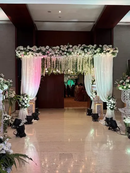 An elegant entrance combining soft white drapes with cascading floral arrangements. This design creates a sophisticated and welcoming ambiance for any wedding event.