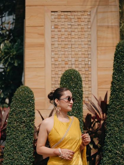 The bride looking chic and stylish in sunglasses and a yellow saree during her outdoor Haldi ceremony.