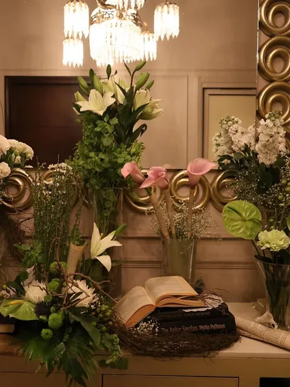 A detailed view of a floral and literature themed decor setup. We combined fresh white lilies, baby's breath, and green anthuriums with vintage books and scrolls to create a sophisticated and story-driven centerpiece arrangement.