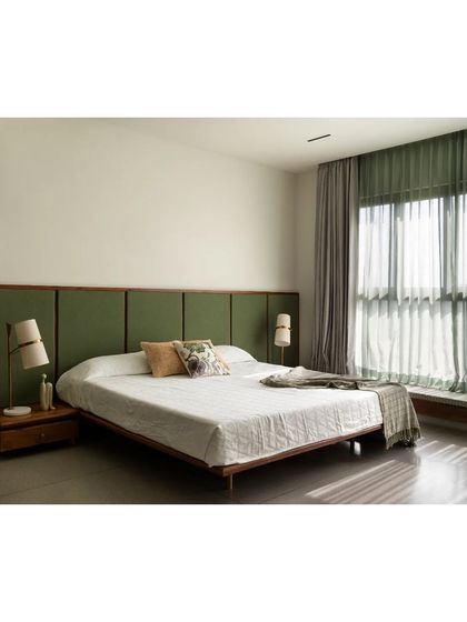 In this master bedroom, the grey terrazzo floor provides a cool, monolithic base for the custom teak bed and moss-green fabric headboard. The material choices are designed to create a feeling of tranquility and groundedness.