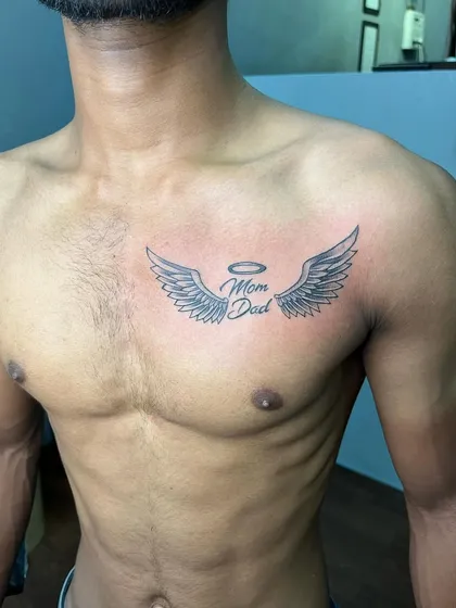 A clean and well-executed "Mom Dad" memorial tattoo on the chest. The shading on the wings gives them a soft, feathered look.