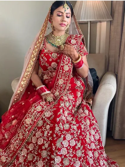 A full view of a classic bridal dream. This bride is wearing a traditional red floral embroidered lehenga, paired with a beautiful green beaded Kundan necklace set, available to rent for your wedding day.