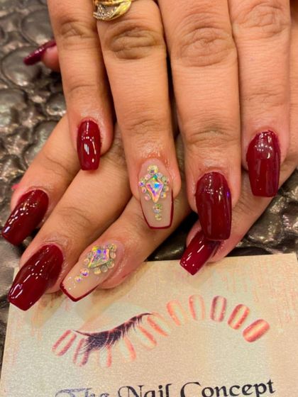 A luxurious design with deep red, square-shaped nails. The accent nails have a sheer base and are adorned with large, iridescent geometric crystals.