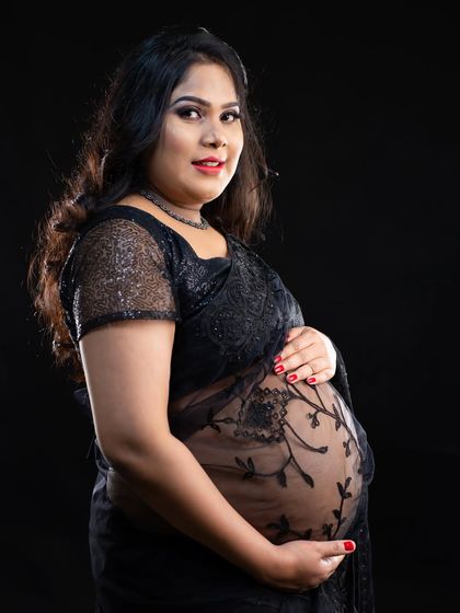 A bold and beautiful portrait in a sheer black lace saree. This modern take on traditional wear elegantly showcases the baby bump against a classic black background.