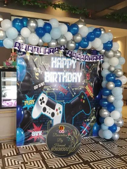 Game on! This is a full view of the gaming-themed birthday backdrop. It features a custom printed banner with controller graphics, framed by a balloon arch in blue, silver, and white to create an exciting zone for the kids.