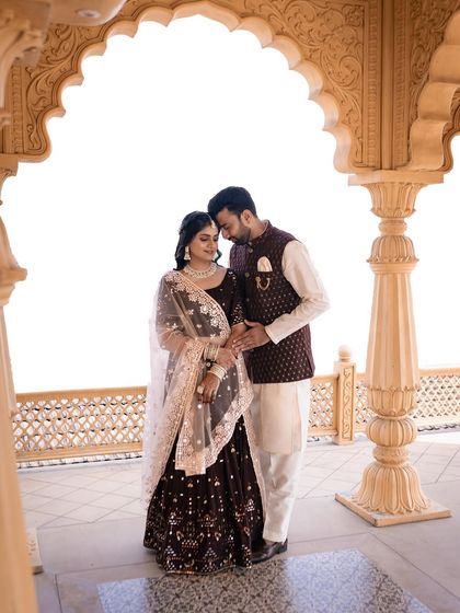 A romantic portrait of the couple. The bride's makeup is soft and elegant, with a focus on flawless skin, perfect for her deep wine colored lehenga and the architectural backdrop.