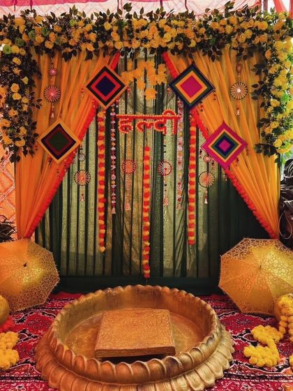 For a classic and colorful Haldi ceremony, I designed this stage using bright yellow and green drapes. The setup is framed with a floral border and features hanging decorative elements above a traditional brass urli.