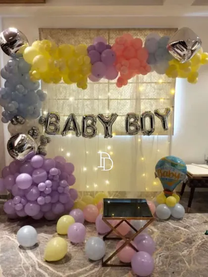 This "BABY BOY" home decoration uses a curtain of fairy lights as a backdrop for the foil balloons. The pastel balloon frame adds color and softness, creating a lovely photo spot.
