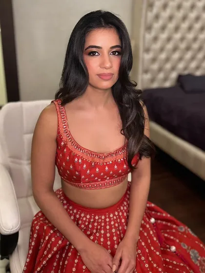 A guest ready for a wedding function in a vibrant red lehenga. We gave her a soft glam makeup look with defined eyes and styled her dark hair in classic, voluminous waves.