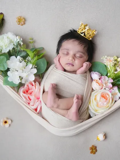 A beautiful overhead shot of a newborn sleeping peacefully in a fabric hammock, adorned with a tiny crown and surrounded by flowers. This pose is perfect for capturing their delicate features in a creative way.