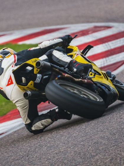 A rider on a yellow superbike seen from behind, perfectly hitting the apex of a corner with the red and white kerbs. This is textbook cornering.