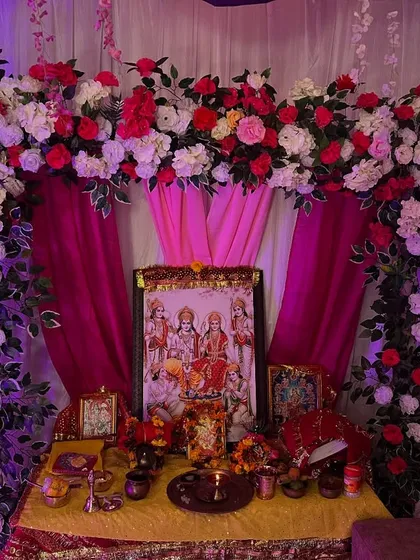 A beautiful floral arch with pink drapes created for a home pooja. The setup provides a perfect frame for the deity's picture.