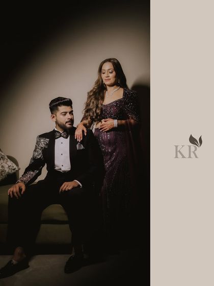 A formal, posed portrait of the couple, showcasing their coordinated outfits and regal presence. The lighting is dramatic and focused.