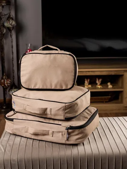 Faborange's packing cubes stacked on an ottoman in a cozy living room setting. This lifestyle image shows how the products can be used for home storage, not just travel.
