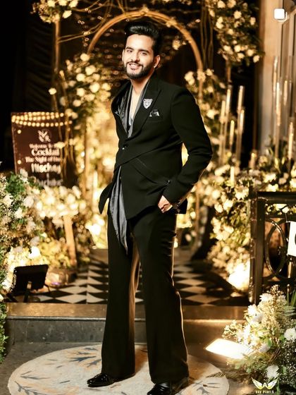 YouTuber Fukra Insaan styled in our unique black cocktail suit for his brother's wedding. The outfit features an asymmetric wrap-style blazer with a draped satin element, creating a modern and edgy silhouette.