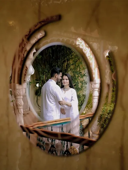 A creatively framed shot of the couple on a balcony, viewed through a circular architectural element. This technique adds an artistic and intimate feel to the portrait.