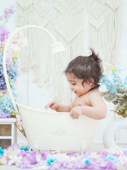 A baby girl explores her flower bath setup. The combination of the tub, flowers, and boho backdrop creates a stunning visual.