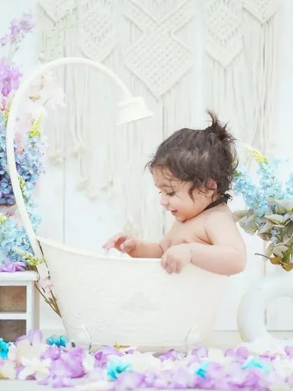 A baby girl explores her flower bath setup. The combination of the tub, flowers, and boho backdrop creates a stunning visual.