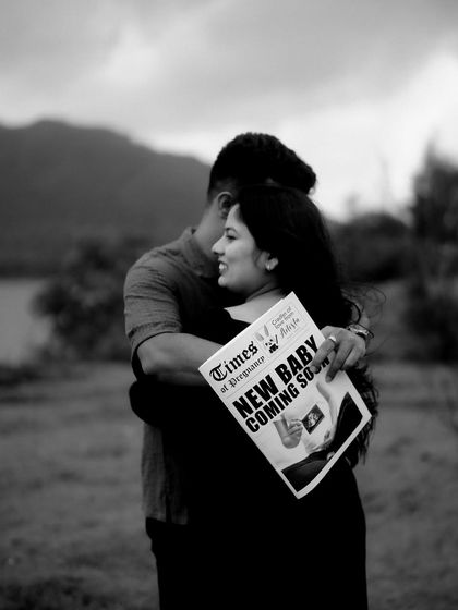 A romantic black and white photo of the couple embracing, holding their announcement newspaper. The focus is on their connection and shared happiness.