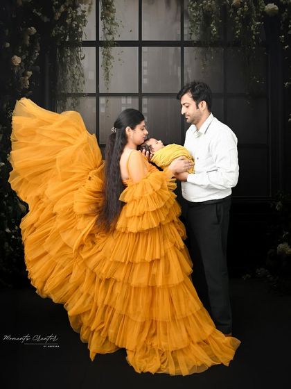 A beautiful silhouette-style portrait of a new family. The parents gaze at their newborn against a window-like backdrop, with the mother's yellow gown adding a pop of vibrant color.