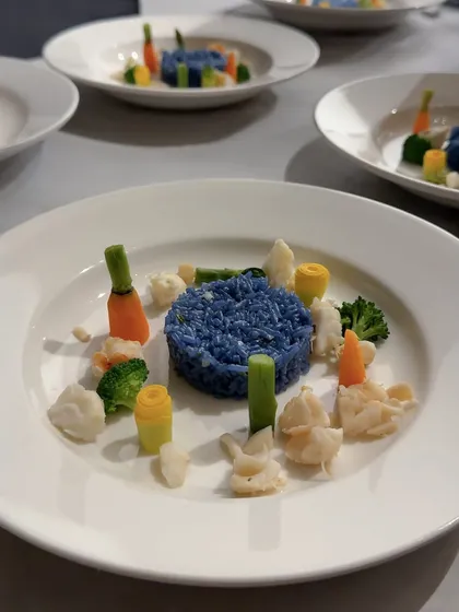 A vibrant dish of blue-pea flower rice with delicately placed vegetables, inspired by the colorful "Stack" sculptures of artist Annie Morris. This plate demonstrates how we translate abstract art into a concrete and delicious culinary form.