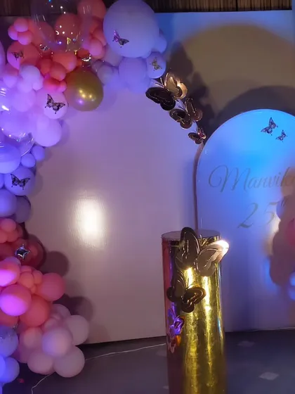 A sophisticated butterfly-themed setup for a 25th birthday, with a pink and purple balloon arch and a golden pedestal for the cake.