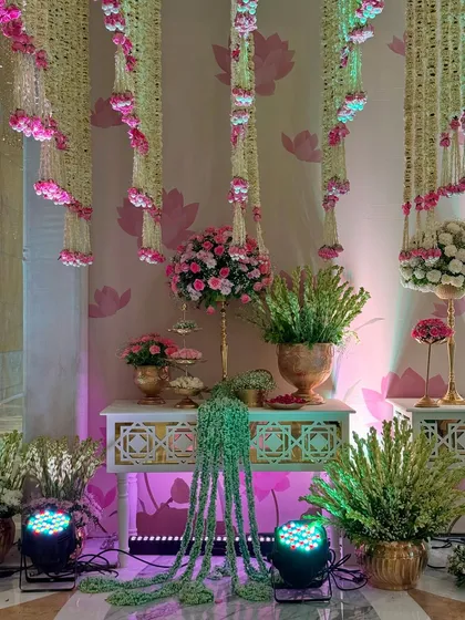 A wider view of a decor corner, where traditional elements are illuminated by soft, colorful lighting. The hanging floral strings and lotus-print wallpaper create a cohesive theme.