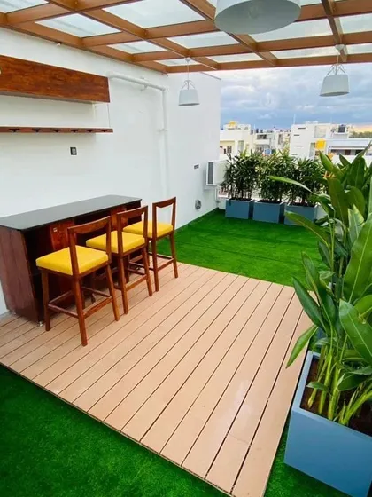 We transformed this rooftop terrace into a chic entertainment zone, complete with a custom bar, WPC wood-look decking, and integrated planters. The glass-topped pergola and modern pendant lighting make it a functional and stylish space, day or night.