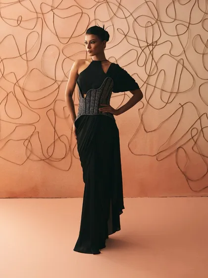 I believe clothes should hold the memory of nights that stretch past midnight. This pre-dstitched sari gown is my interpretation of that feeling, with a sculpted, hand-embroidered corset that anchors the fluid black drape. It is a balance of sharp structure and effortless elegance.