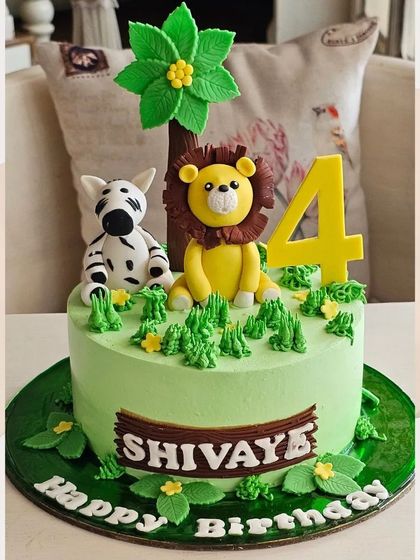 A cute and friendly jungle animal cake with a lion and zebra sitting under a palm tree, perfect for a 4th birthday.