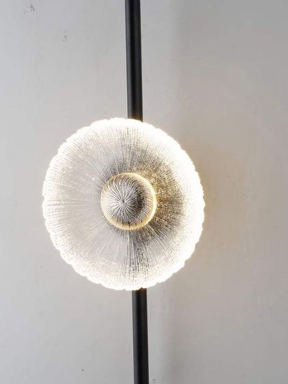 A modern wall sconce with a textured glass disc on a black stem. A simple yet effective design for adding accent lighting.