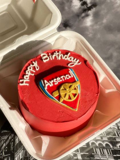 For the sports fan in your life. This bento cake features a hand-piped Arsenal football club logo on a vibrant red background.