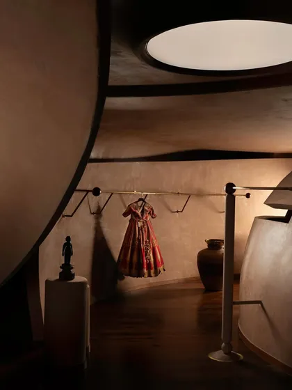 A single garment is displayed like a piece of art against the curving, earthen-toned walls. The architecture acts as a quiet, respectful stage for the couture.