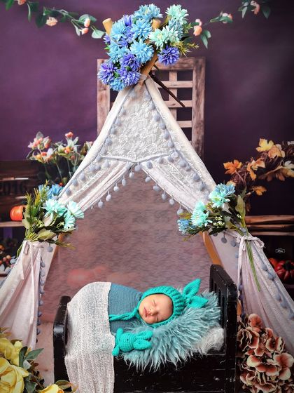 A newborn sleeps soundly in a miniature tent setup, adorned with blue flowers. This whimsical and creative camp theme makes for a unique and memorable baby portrait.