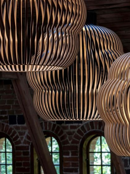 A close-up, low-angle shot of several Kuulto pendants, emphasizing the rhythmic pattern of the wooden slats and the warm light emanating from within.