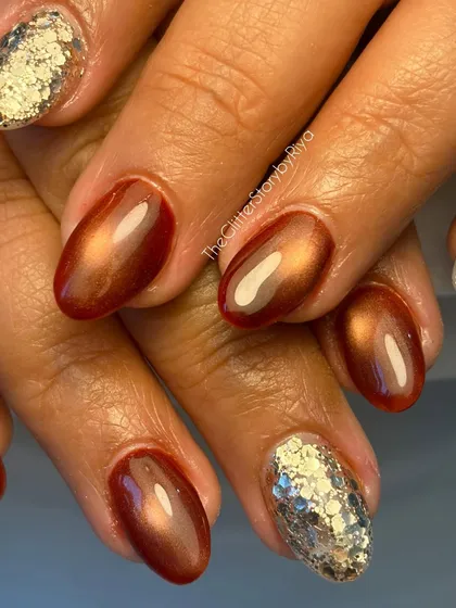 A close-up of a warm, coppery cat-eye manicure. This set is paired with a chunky silver glitter accent nail for a beautiful contrast of textures.