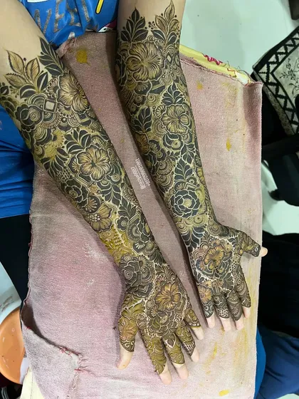 Full coverage bridal henna with a mix of floral and geometric elements. The design is consistent from the fingers to the elbow cuff.