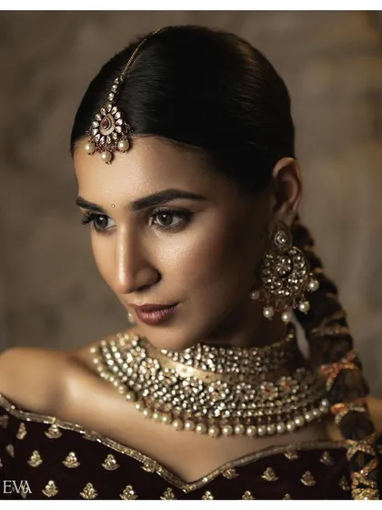 A close-up portrait focusing on the model's elegant profile and traditional jewellery. The soft lighting accentuates the details of the maang tikka, choker, and earrings.