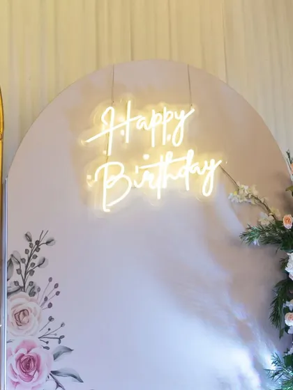 A close-up of the custom "Happy Birthday" neon sign, which added a modern and warm glow to the elegant floral backdrop.