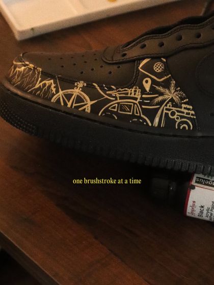 A close-up of the travel icons I painted on the black AF1s. The design includes a car with luggage, a bicycle, palm trees, and a camera, capturing the spirit of adventure.