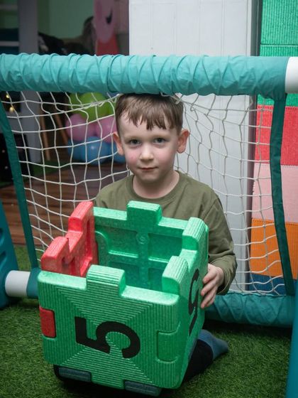 This boy uses a large foam block as part of his game by the soccer net, showing how different play elements can be combined.