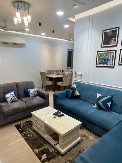 This view reveals the full seating arrangement, featuring a combination of a blue L-shaped sofa and a cozy grey two-seater. This layout provides ample seating for family and guests while maintaining an open and sociable atmosphere.