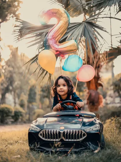 A joyful, full-color shot of a toddler "driving" his toy car during an outdoor birthday session.