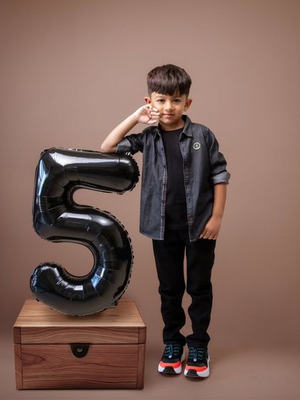Here, the birthday boy is posing with his number five balloon against a simple, warm-toned backdrop. This classic studio portrait focuses on his calm and cool demeanor, showing a different side of his personality as he marks this important milestone.