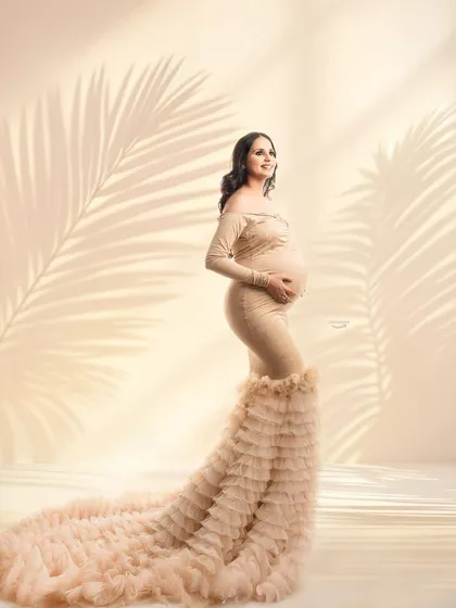 This portrait showcases a gorgeous beige gown with a dramatic ruffled train. The soft lighting and subtle palm leaf shadows create a warm, almost tropical feel in this studio setup.