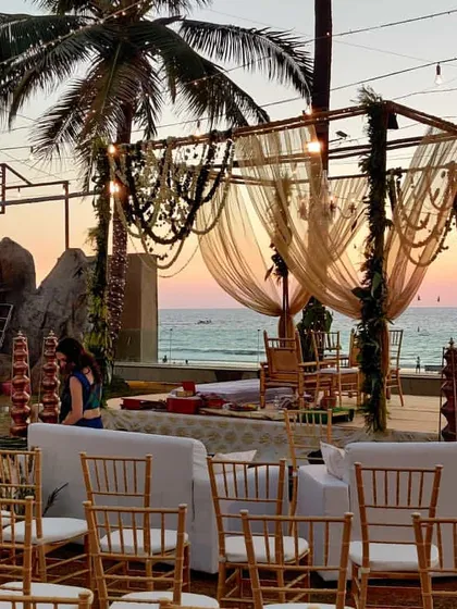 This rustic mandap design uses natural elements like wooden poles and decorative beaded hangings. The setup is enhanced by comfortable white sofas for family seating, creating a relaxed and intimate vibe.