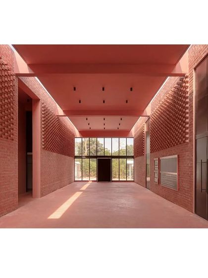 Inside the memorial's main hall, the textured brick walls and high ceiling create a serene and contemplative atmosphere. The large glass opening at the end frames a view of the landscape, connecting the interior to the outside.