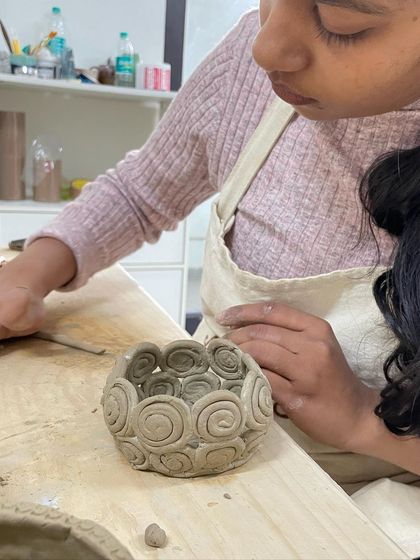 This student is building a pot using the coiling method, adding decorative spirals to the outside for a unique, textured look.