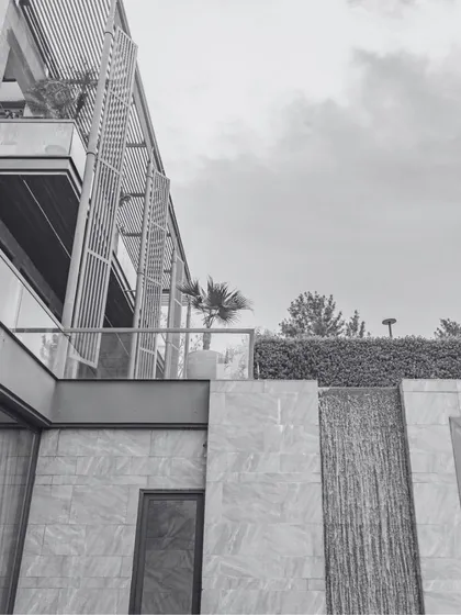 A black and white detail shot of a luxury residence, emphasizing the architectural lines and textures. The modern facade with its louvered screens and stone cladding showcases our focus on creating a harmonious blend of materials and forms.